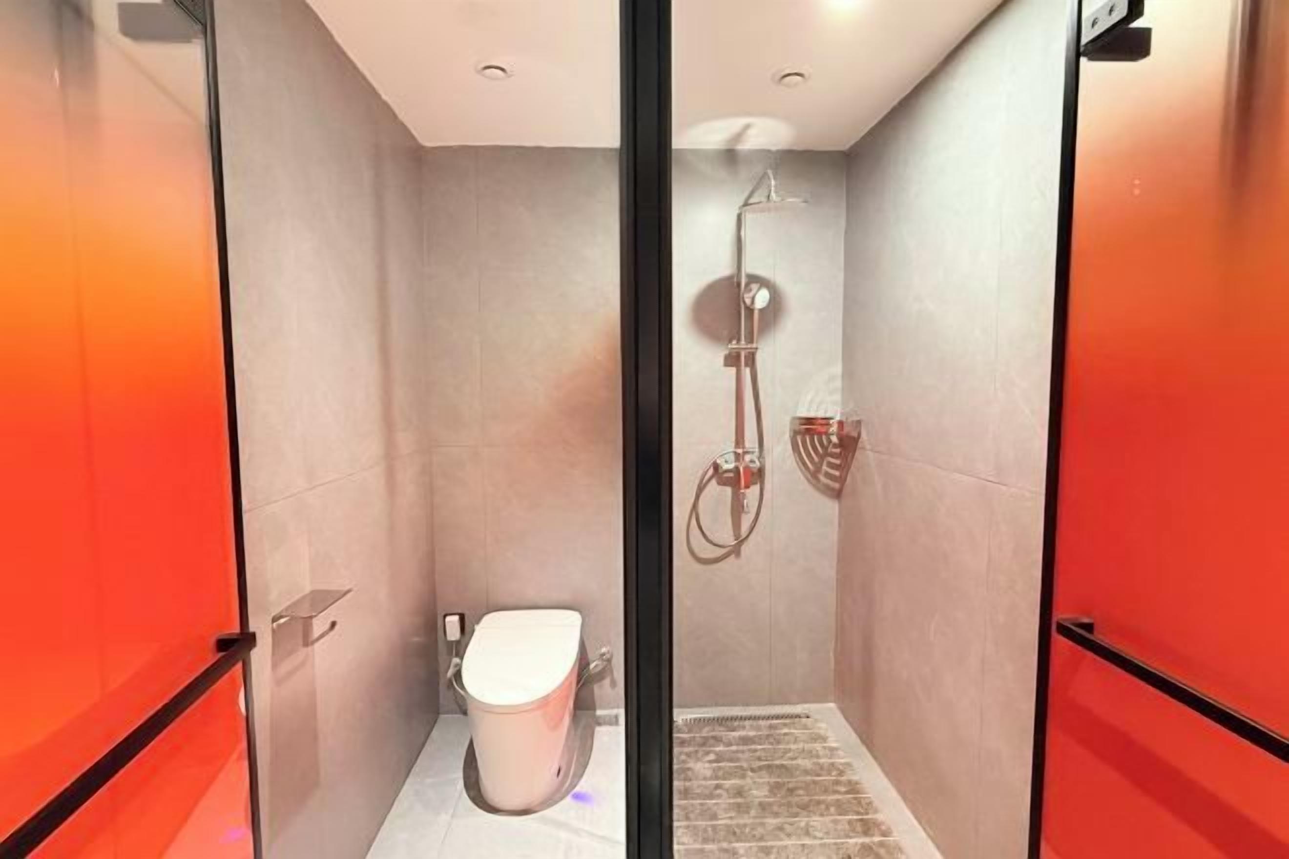 Et moderne badeværelse med glasvæg, toilet, bruseområde og en rød dør.