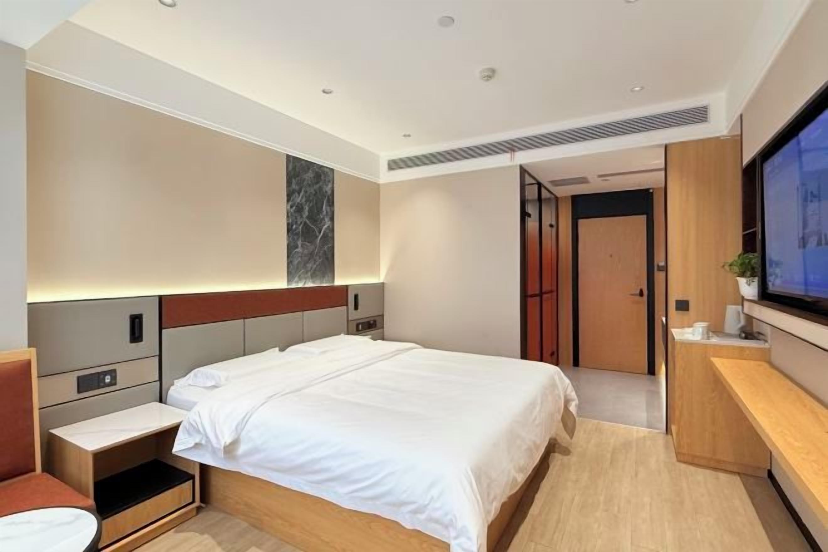 A modern hotel room with a large bed, bedside tables, a TV, and a wooden floor.