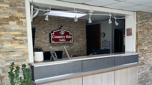 A reception desk with a sign reading "Country Side Suites," a clock, and a potted plant. - Countryside Suites Kansas City Independence I-70E Sports Complex Hotel (Independence)