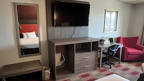 A hotel room with a bed, a desk with a chair, a TV mounted on the wall, a mirror, and a window with a view. - Countryside Suites Kansas City Independence I-70E Sports Complex Hotel (Independence)