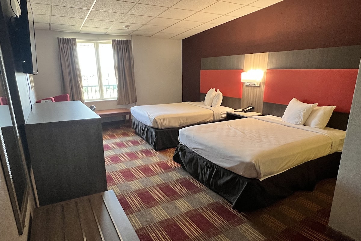 A hotel room with two single beds, a desk, a chair, a TV, and a window with curtains.
