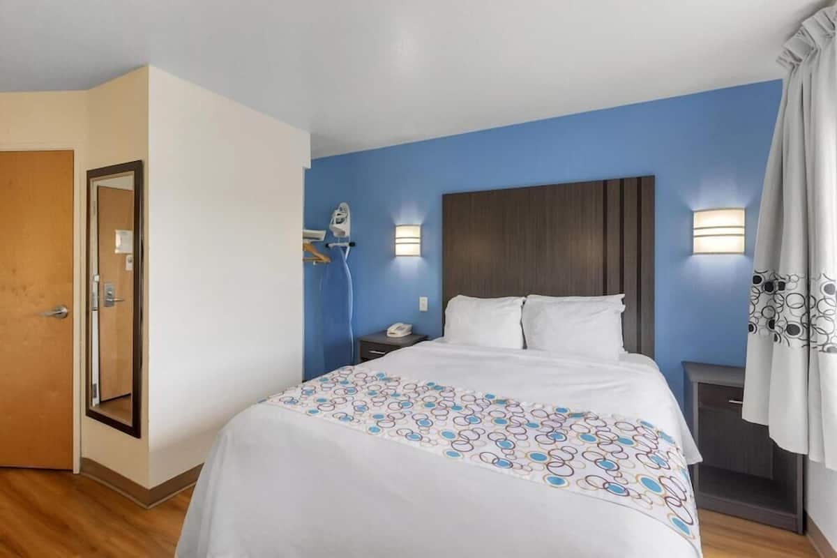 Une chambre d’hôtel comprenant un lit, une table de chevet, un miroir, une lampe fixée au mur et une porte.