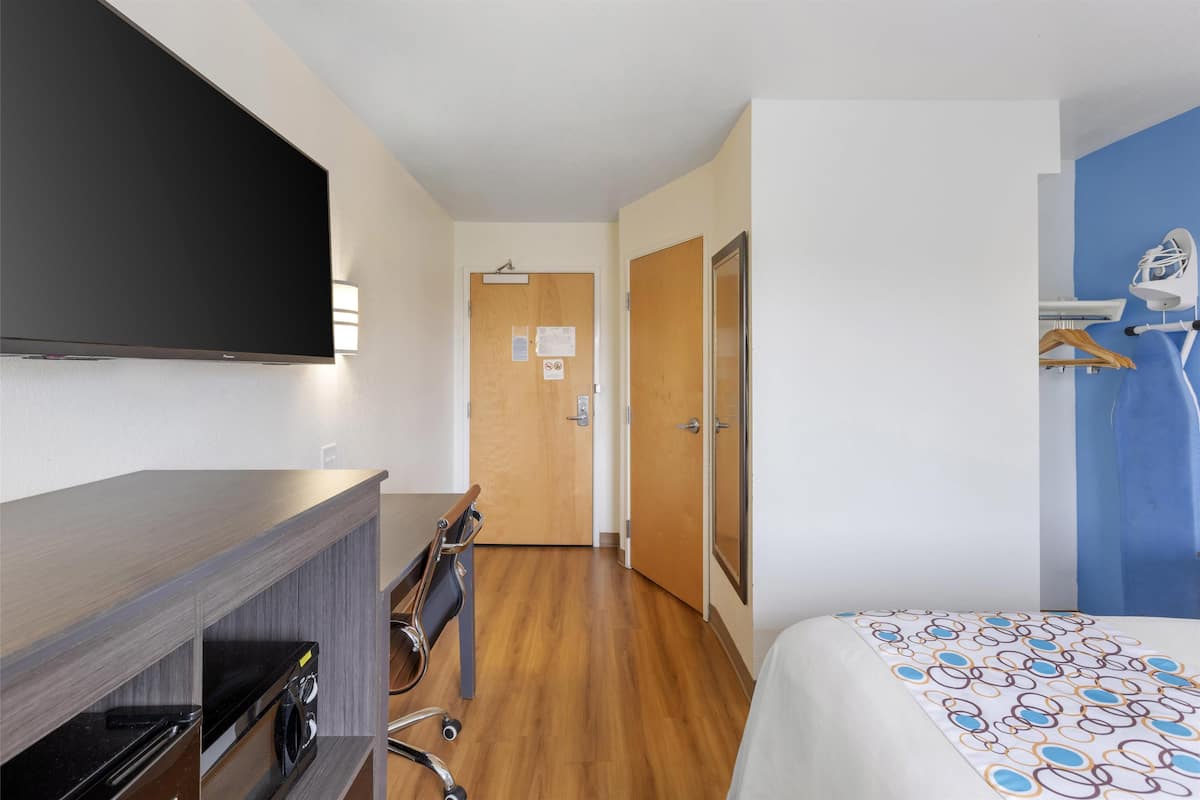 Une chambre d’hôtel équipée d’un lit, d’une télévision, d’un bureau avec un ordinateur, d’une machine à laver et d’un espace douche.