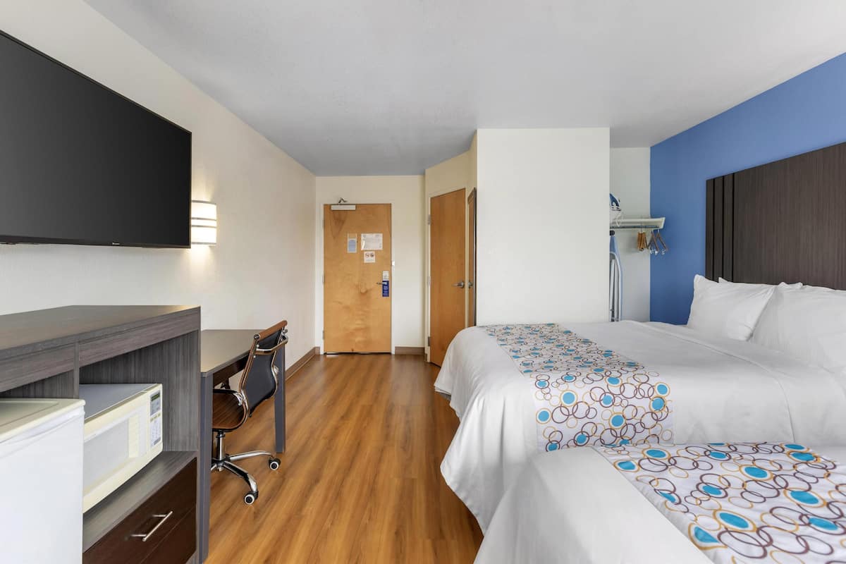 Une chambre d’hôtel comprenant un lit, un bureau avec un ordinateur, une télévision et une porte donnant sur une autre pièce.