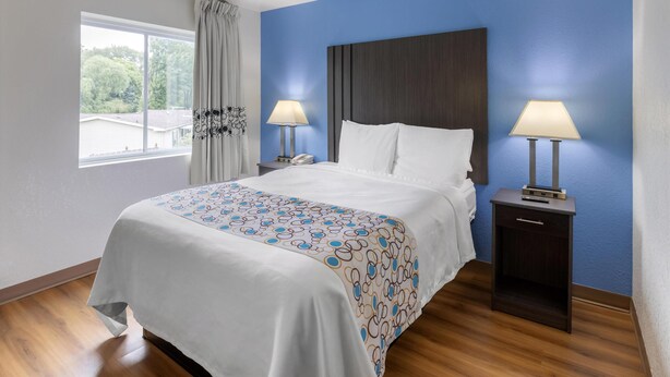 Habitación de hotel con una cama grande, dos mesitas de noche con lámparas, una ventana con cortinas y vistas al exterior con vegetación.
