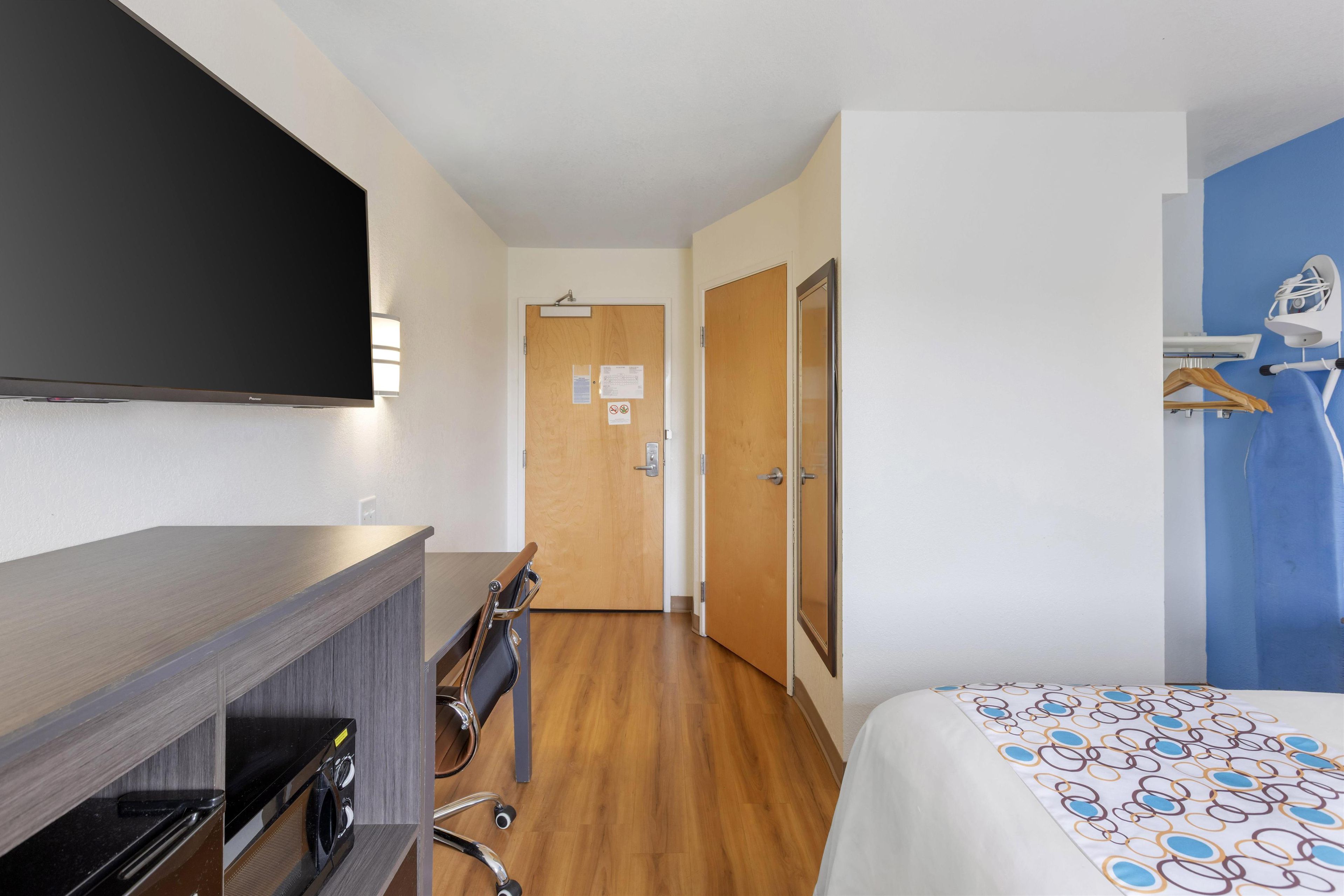 A hotel room with a bed, a TV, a desk with a computer, a washing machine, and a shower area.