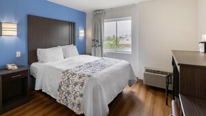 Una habitación de hotel con cama, mesita de noche, lámpara y ventana con vistas.