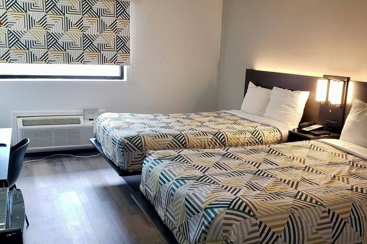 A hotel room with two beds, a desk, and a window with a geometric pattern.