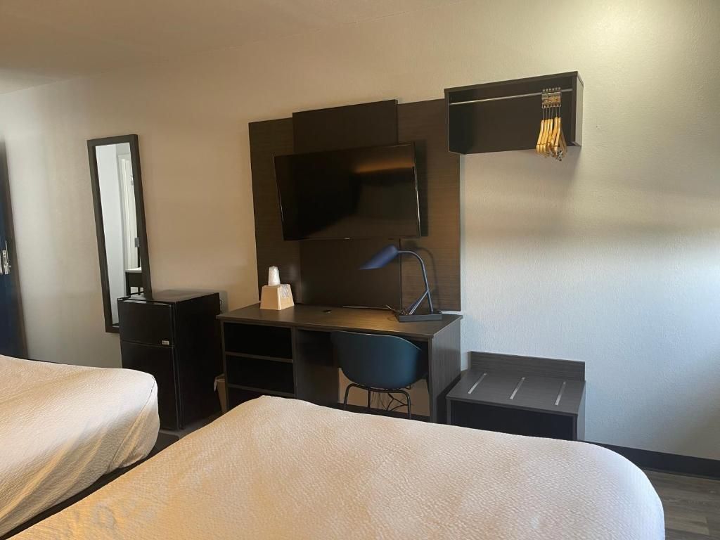 A hotel room with a bed, a desk with a chair, a mirror, and a television.