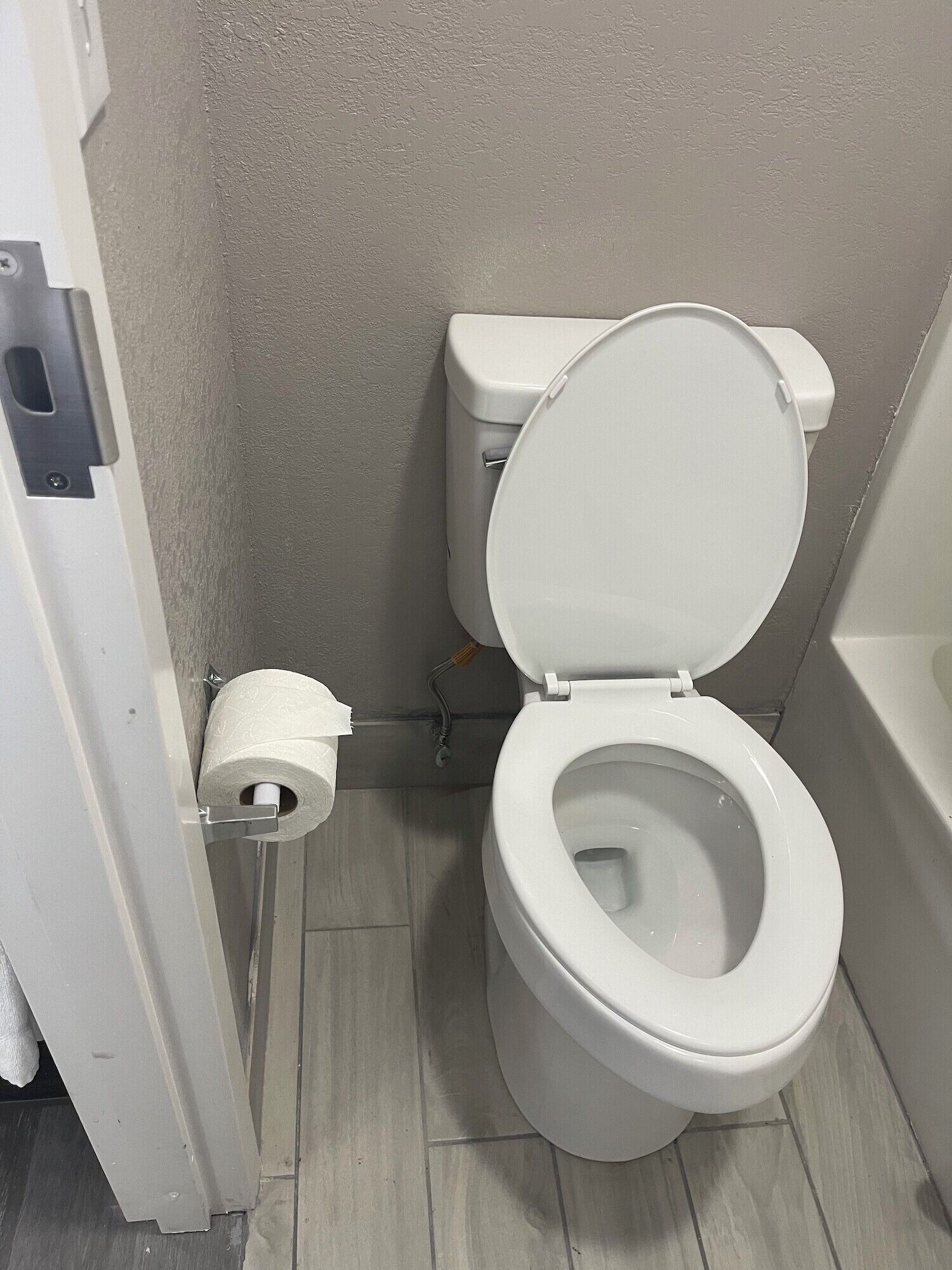 A white toilet with a closed lid in a bathroom with grey walls and wooden flooring.