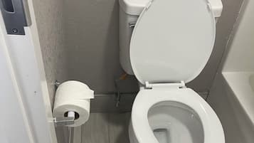 A white toilet with a closed lid in a bathroom with grey walls and wooden flooring.