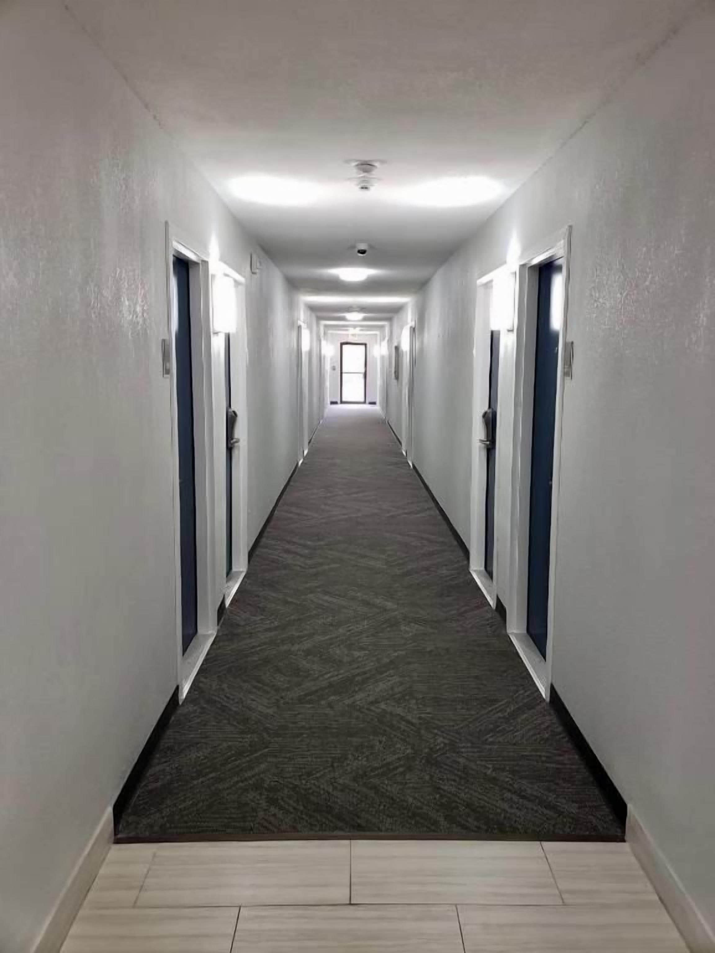 A long, narrow hallway with doors on both sides, leading to a bright room at the end.