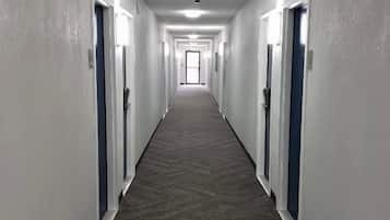 A long, narrow hallway with doors on both sides, leading to a bright room at the end.
