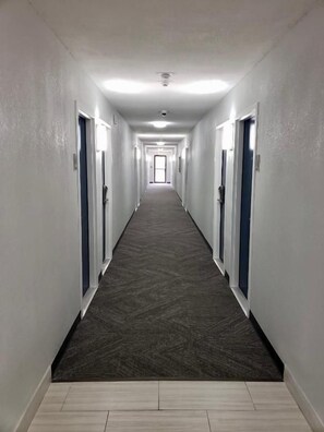A long, narrow hallway with doors on both sides, leading to a bright room at the end. - Motel 6 East Ridge, TN (Chattanooga)