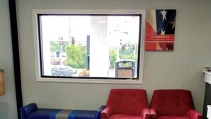 Une salle d’attente avec deux canapés rouges et un canapé bleu, une grande fenêtre donnant sur la rue et une affiche accrochée au mur.