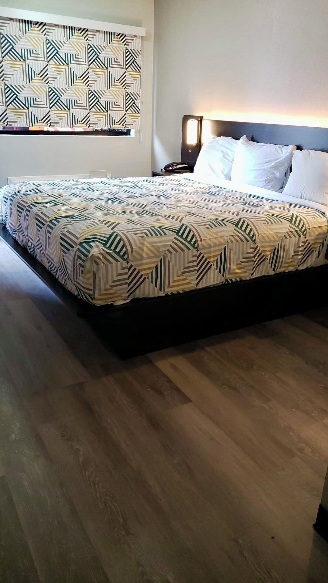 Et soveværelse med et mønstret sengetæppe, et natbord med en lampe og en væg med et geometrisk design.