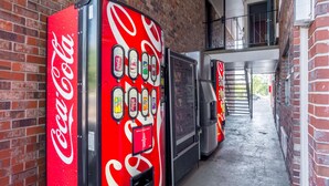 Un distributeur automatique de Coca-Cola situé dans une ruelle bordée de murs en briques et dotée d’un escalier en métal.