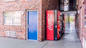 Un bâtiment en briques avec une porte bleue, un distributeur automatique de Coca-Cola et une fenêtre sur laquelle est affiché un panneau.