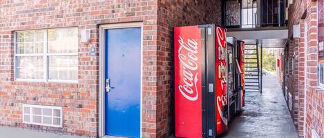 En murstensbygning med en blå dør, en Coca-Cola automat og et vindue med et skilt.