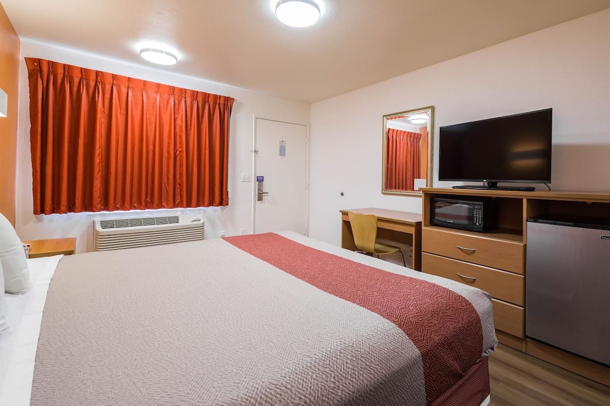 A hotel room with a bed, a desk, a television, a microwave, and a refrigerator.