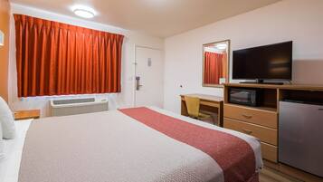 A hotel room with a bed, a desk, a television, a microwave, and a refrigerator.
