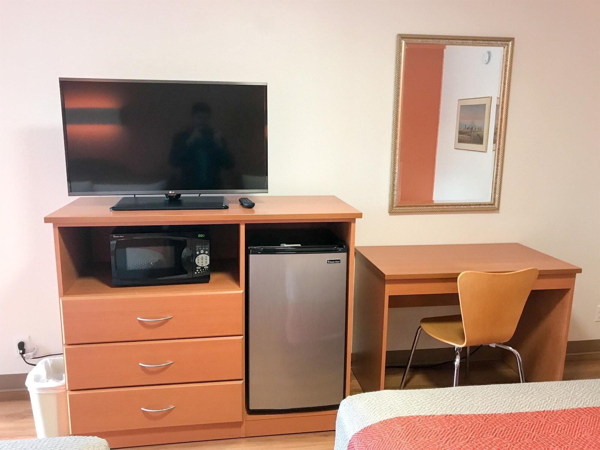 A compact room with a bed, a desk with a chair, a television, a microwave, and a refrigerator.