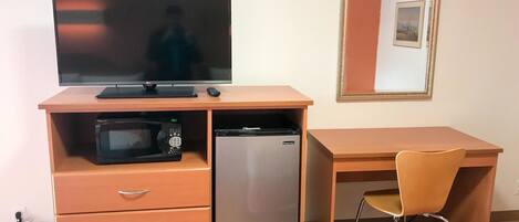 A compact room with a bed, a desk with a chair, a television, a microwave, and a refrigerator.