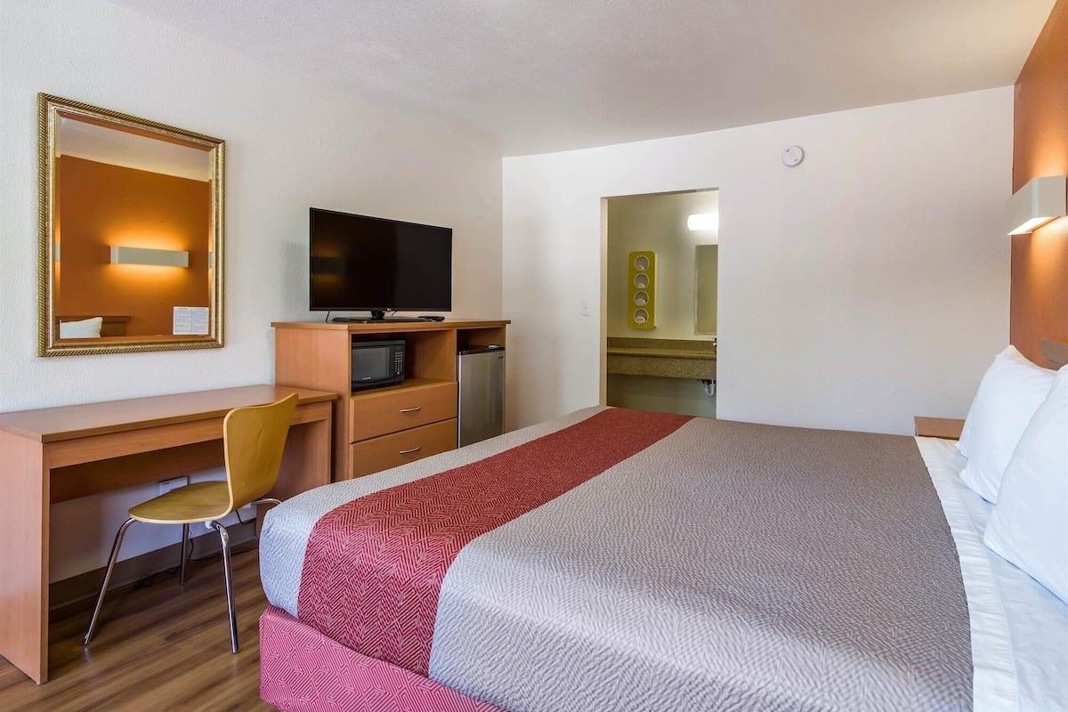 A hotel room with a bed, a desk with a chair, a television, and a mirror.