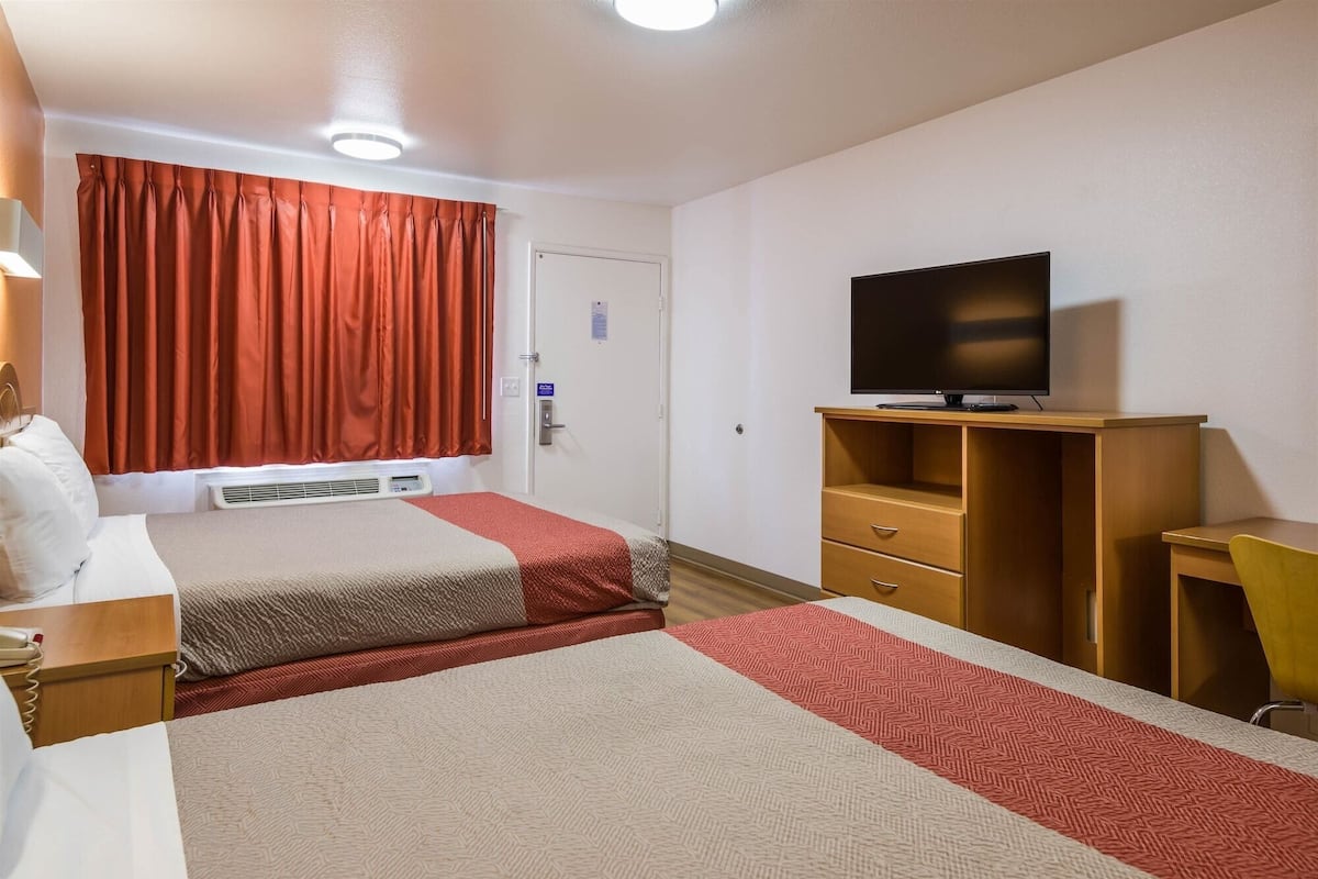 A hotel room with two beds, a TV on a wooden stand, a desk, and a chair.