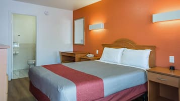 Habitación de hotel con cama, mesitas de noche, un espejo y un baño visible a través de una puerta abierta.