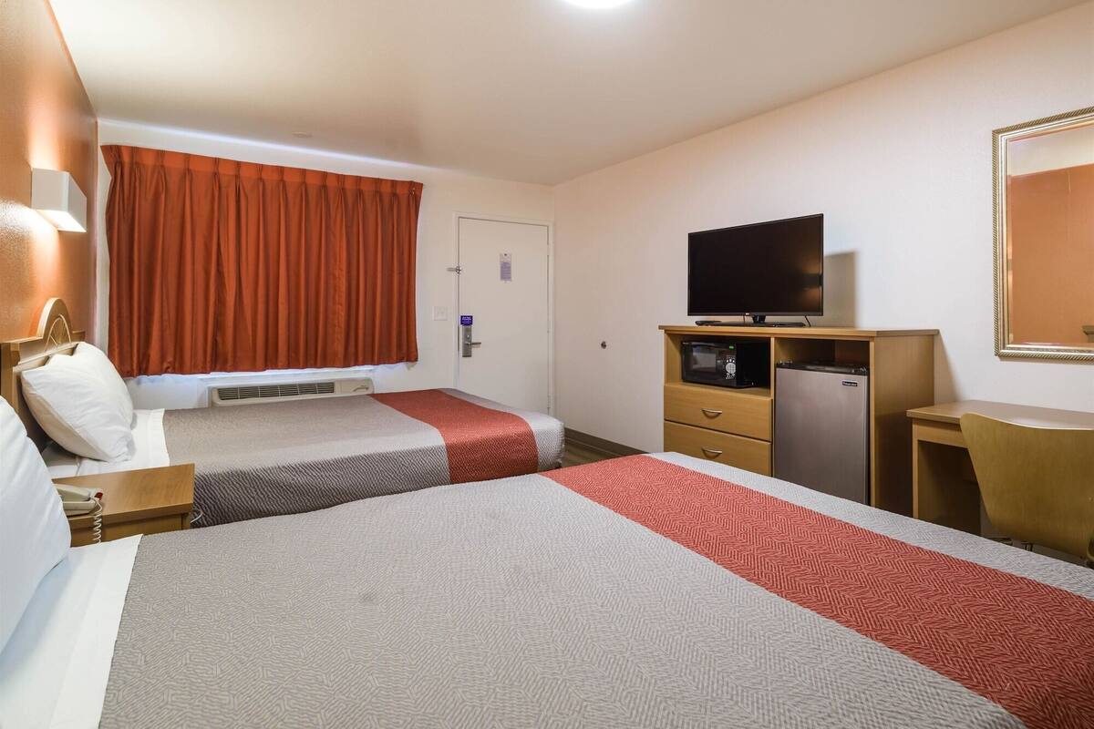 A hotel room with two beds, a television, a desk, and a refrigerator.