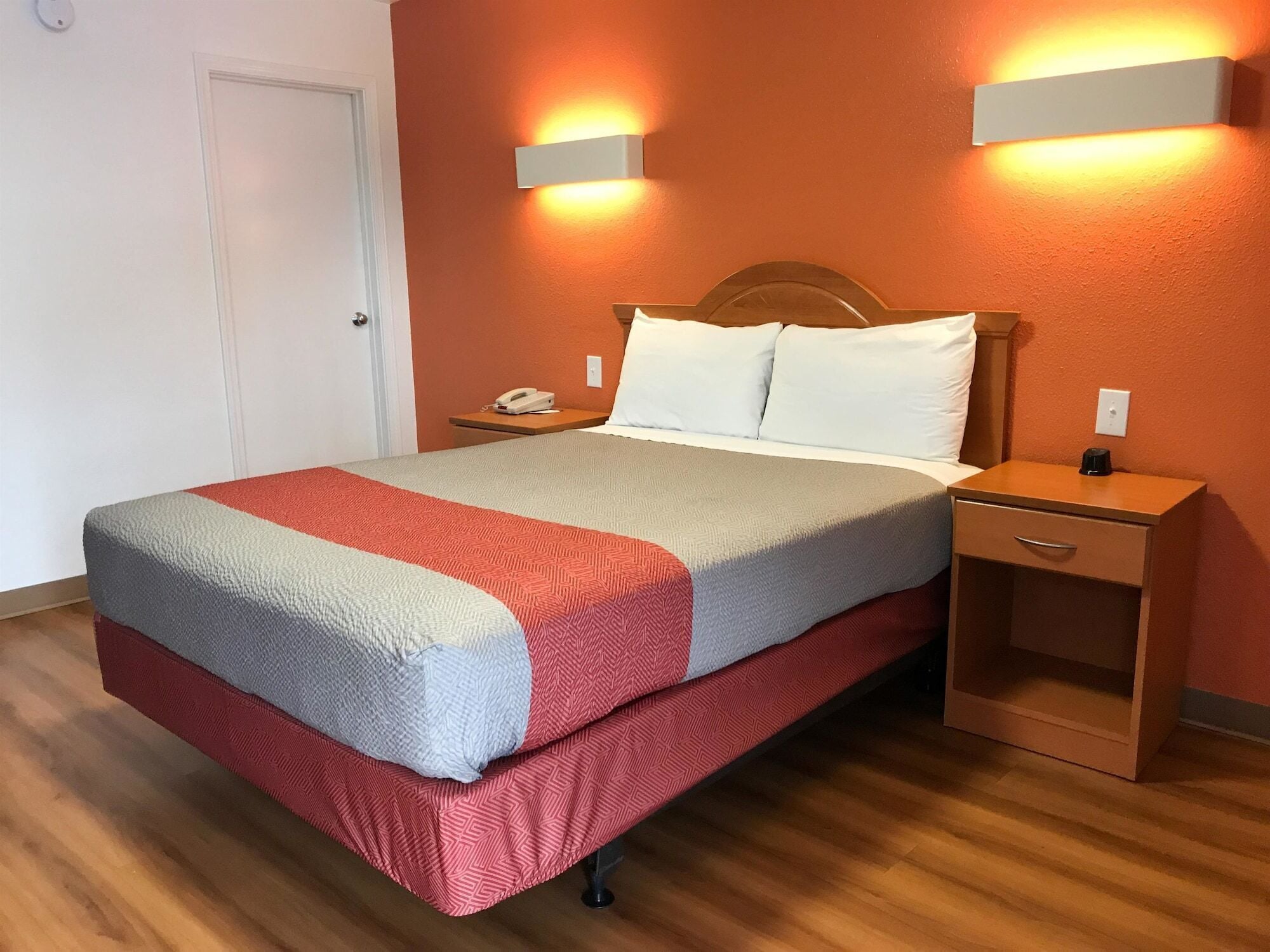 A neatly made bed with a red and grey bedspread, two bedside tables with lamps, and a wooden headboard.