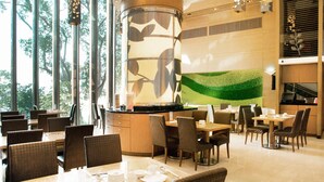 A modern restaurant with large windows, a central decorative column, and a green wall mural. - Royal View Hotel (Tsuen Wan)