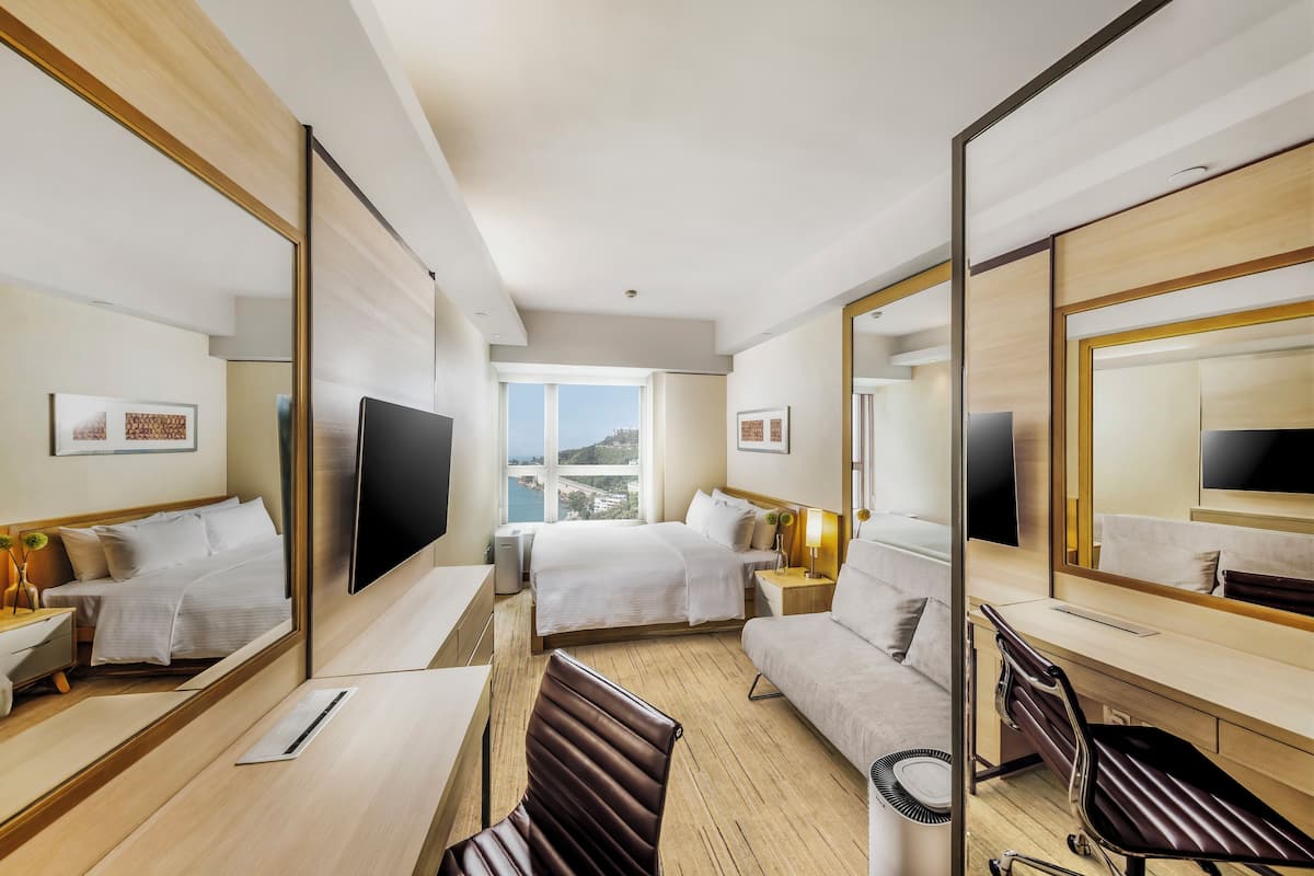 Une chambre d’hôtel avec un lit, un bureau, une chaise, une télévision et un grand miroir.