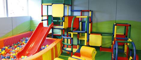 Zona de juegos con tobogán, estructuras para escalar y superficies blandas.