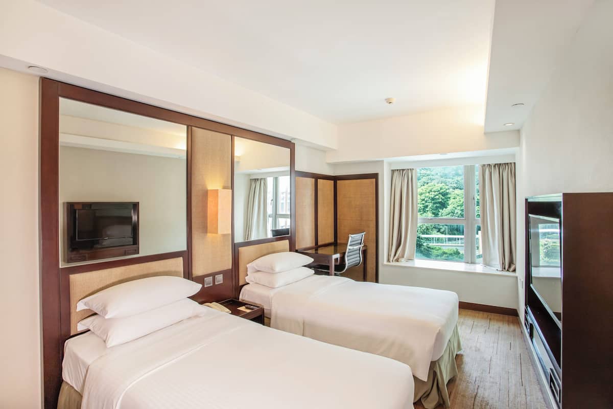 Une chambre d’hôtel avec deux lits, une télévision, un bureau et une grande fenêtre avec des rideaux.