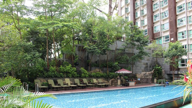 A swimming pool with lounge chairs and a rock wall. - Royal View Hotel (Tsuen Wan)