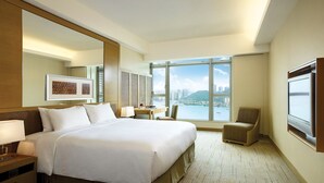 A hotel room with a large bed, a desk, a chair, and a view of a cityscape through large windows. - Royal View Hotel (Tsuen Wan)