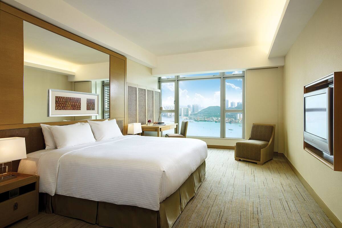 Une chambre d’hôtel avec un grand lit, un bureau, une chaise et une vue sur le paysage urbain, grâce à de grandes fenêtres.