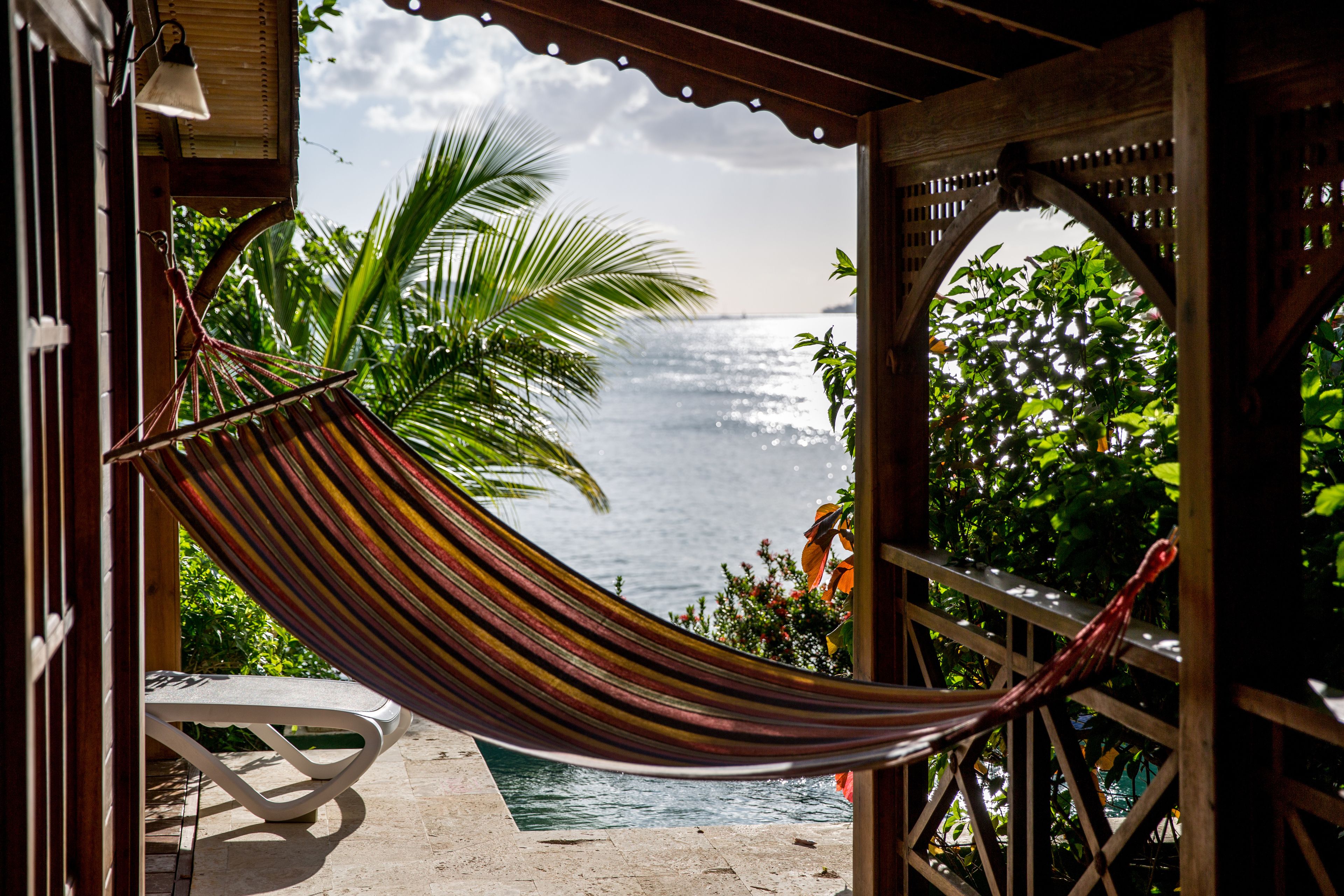 A hammock tied between wooden posts, overlooking a pool and a view of the ocean.