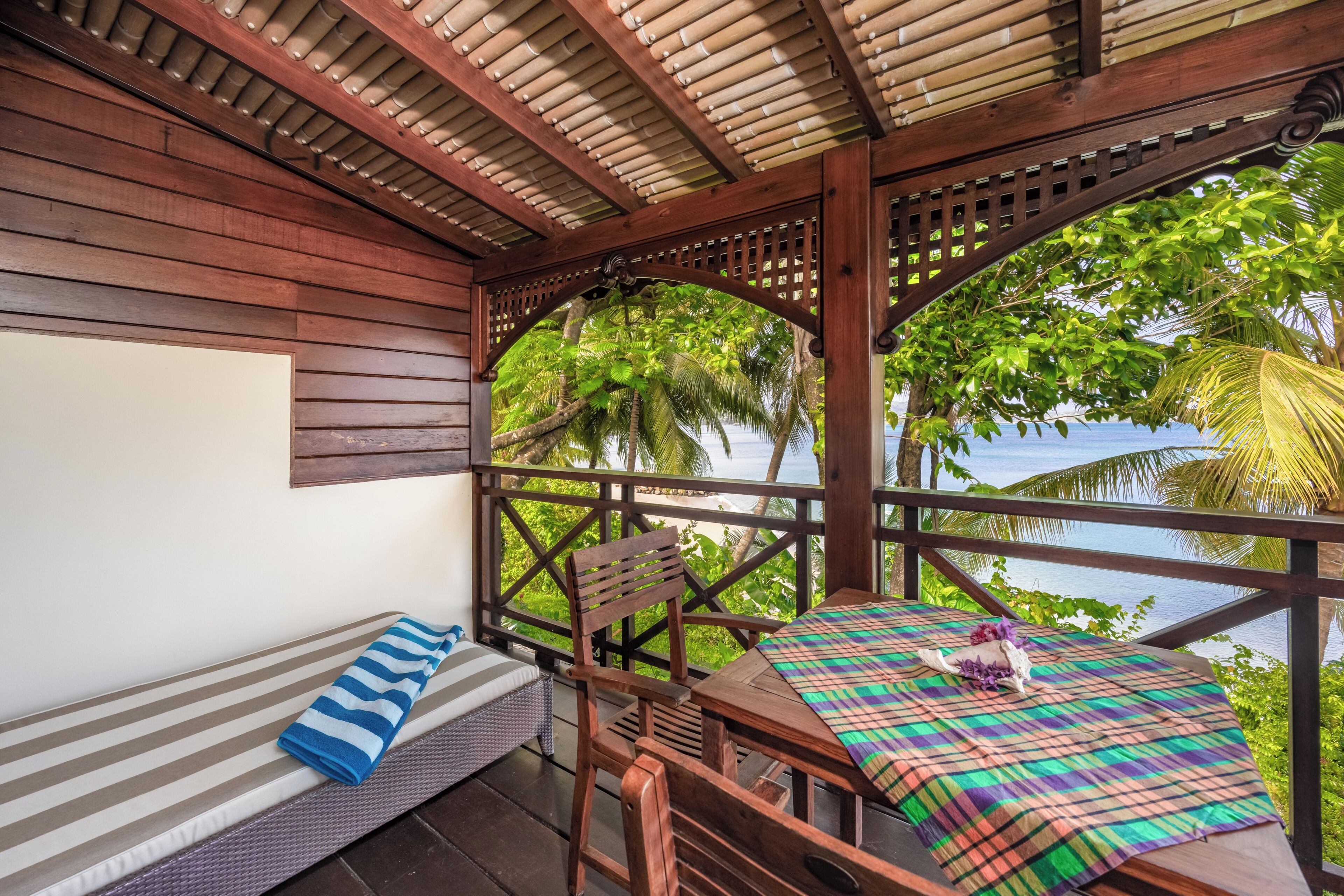 A wooden deck with a bench and a table, overlooking a tropical beach and ocean.