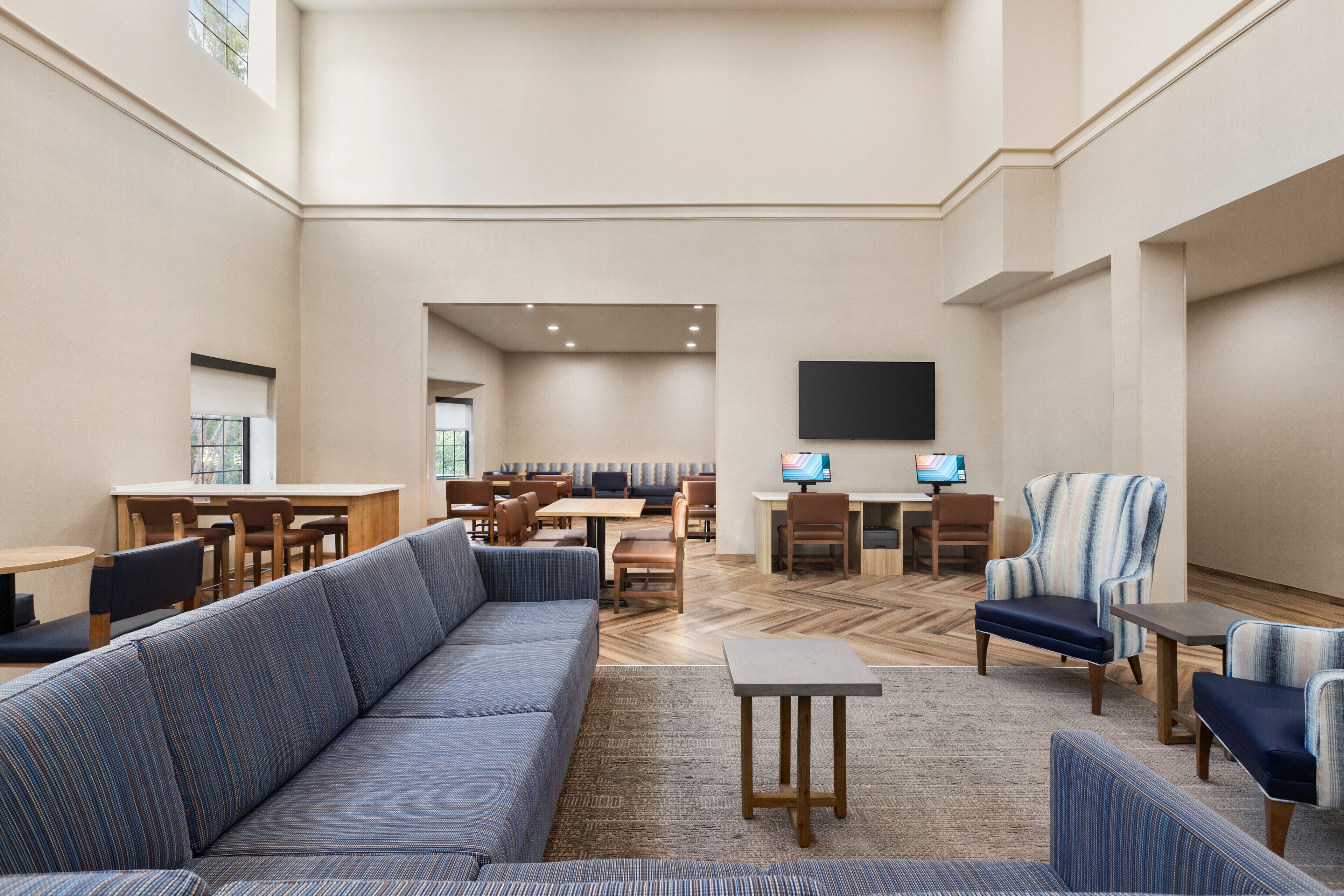 A spacious lobby with a large sofa, multiple seating areas, and a flat-screen TV mounted on the wall.