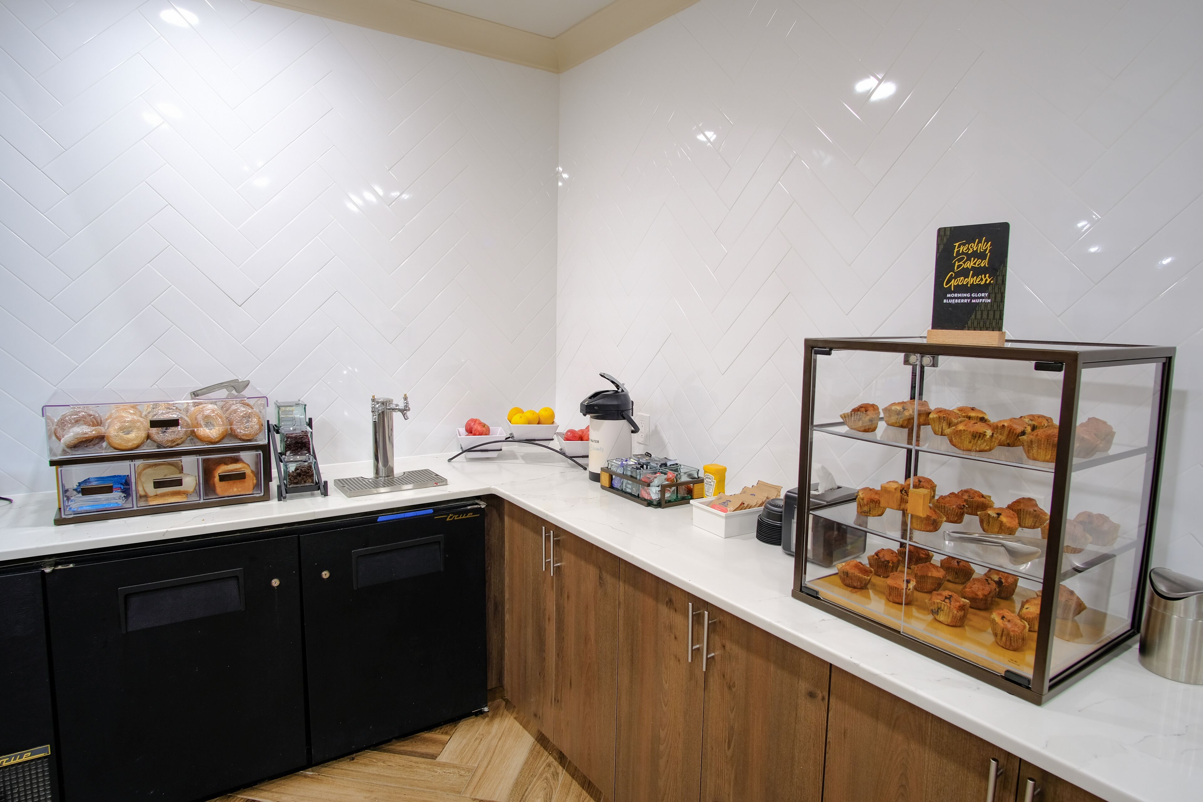 A kitchen with a display case of baked goods, a coffee machine, and a food display with various items.