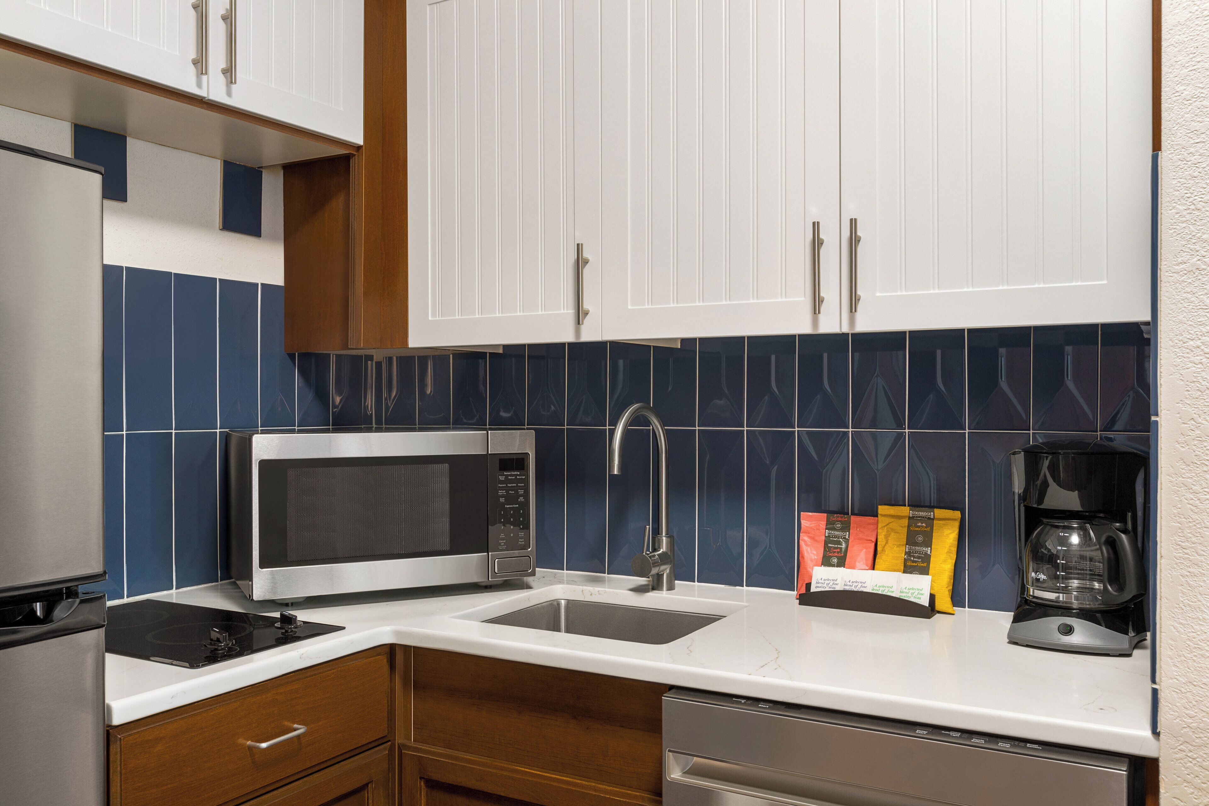 A modern kitchen with white cabinets, a microwave, a coffee maker, and a sink.
