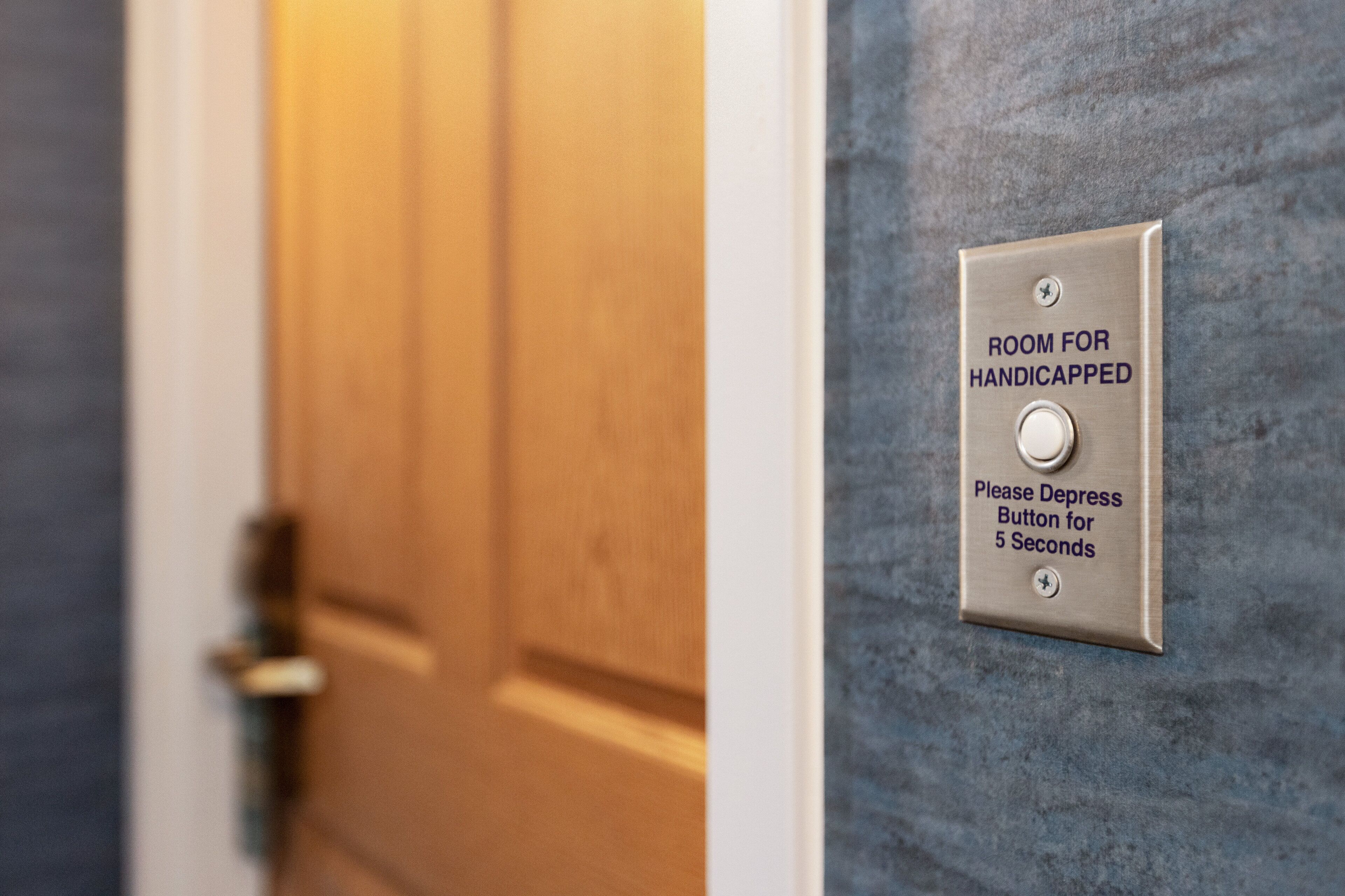 A sign indicating a room for handicapped individuals with instructions to depress the button for 5 seconds.