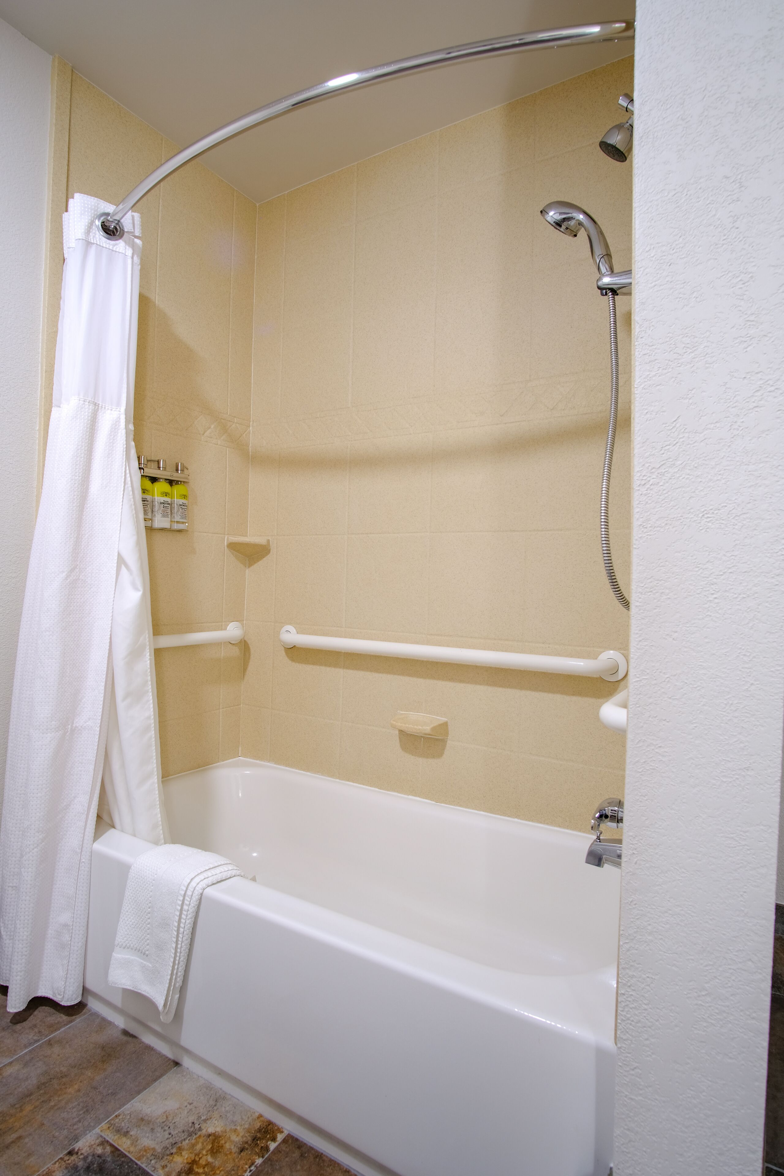 A standard hotel bathroom with a bathtub, shower, and grab bars.