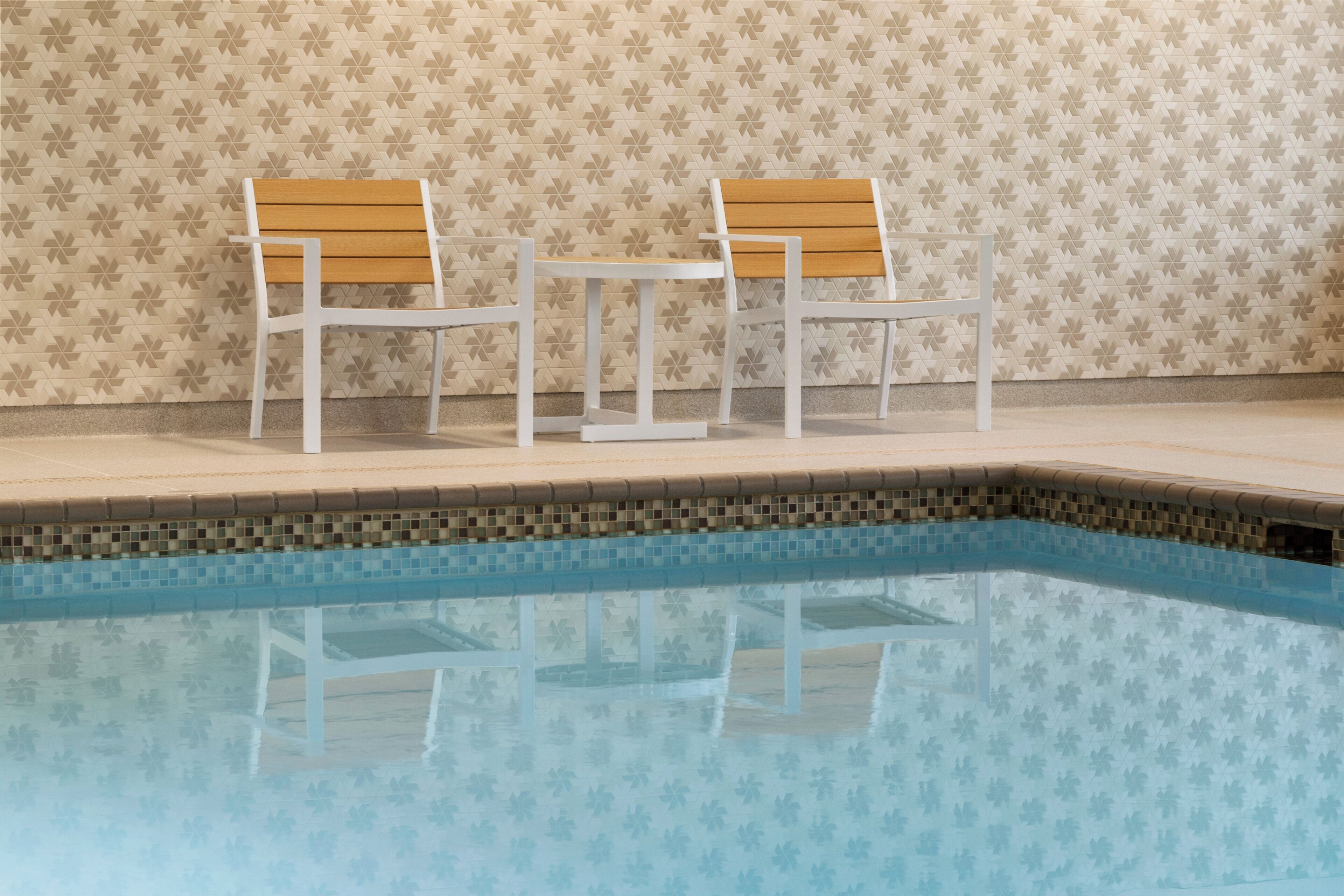 A swimming pool with two white chairs and a wooden bench.