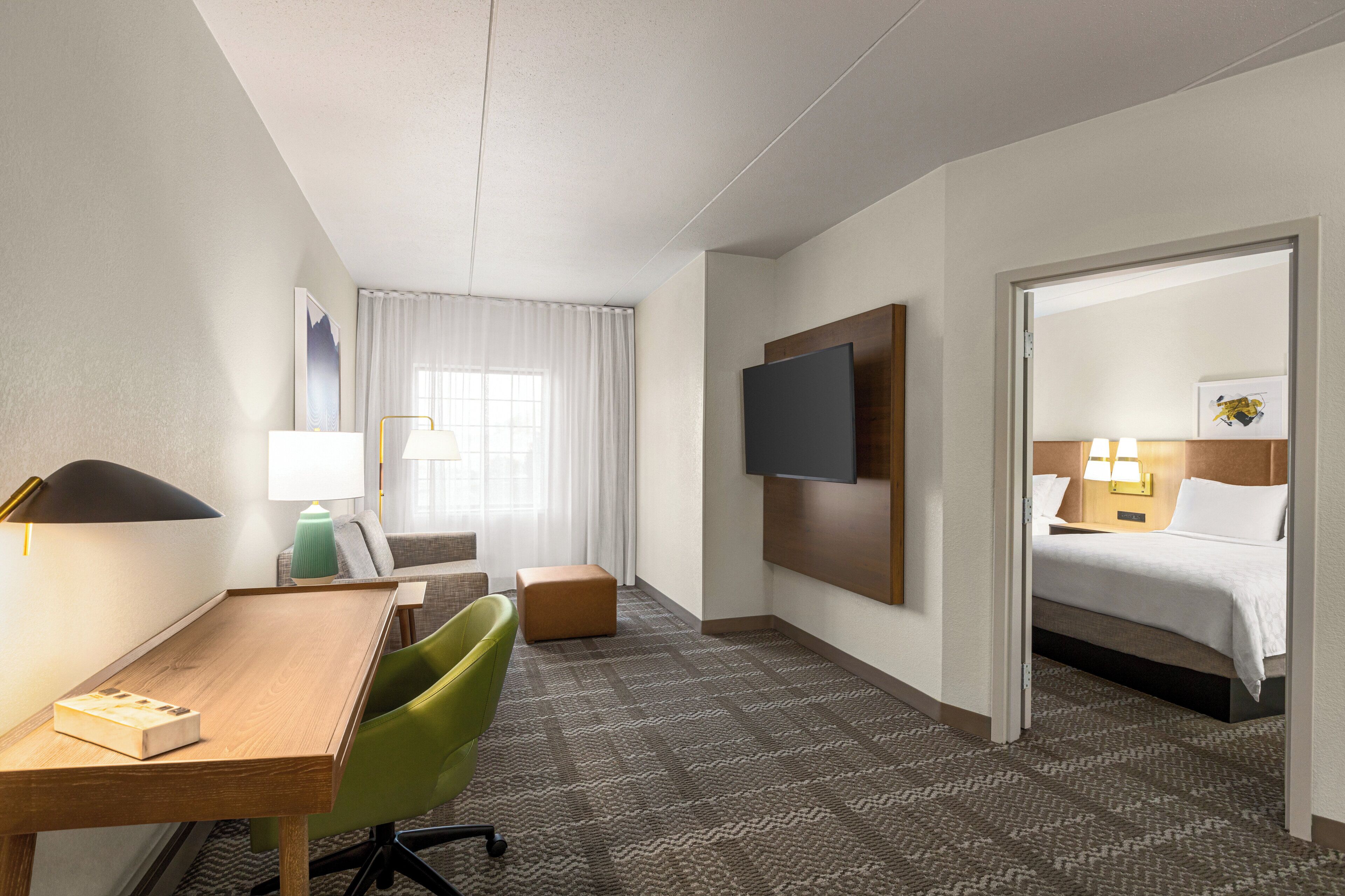 A hotel room with a desk, chair, sofa, TV, and a bed.