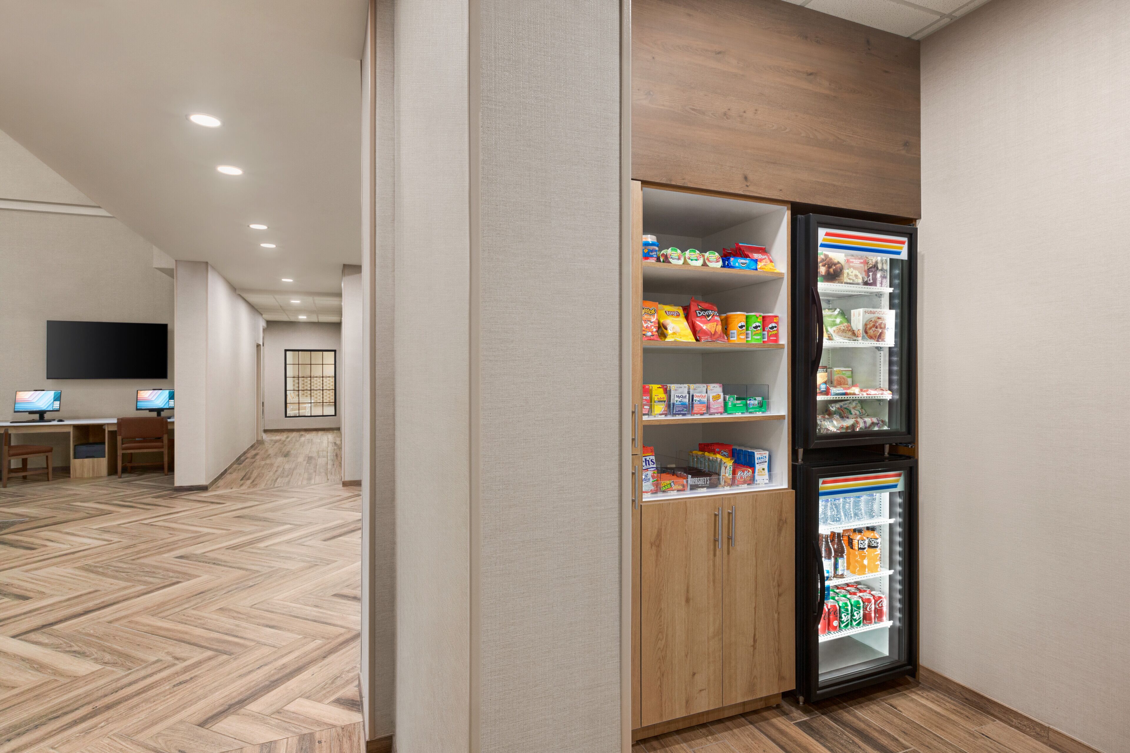 Un hall d’hôtel doté d’un plancher en bois, d’un espace détente avec des tables et des chaises, et d’un distributeur automatique de collations et de boissons.