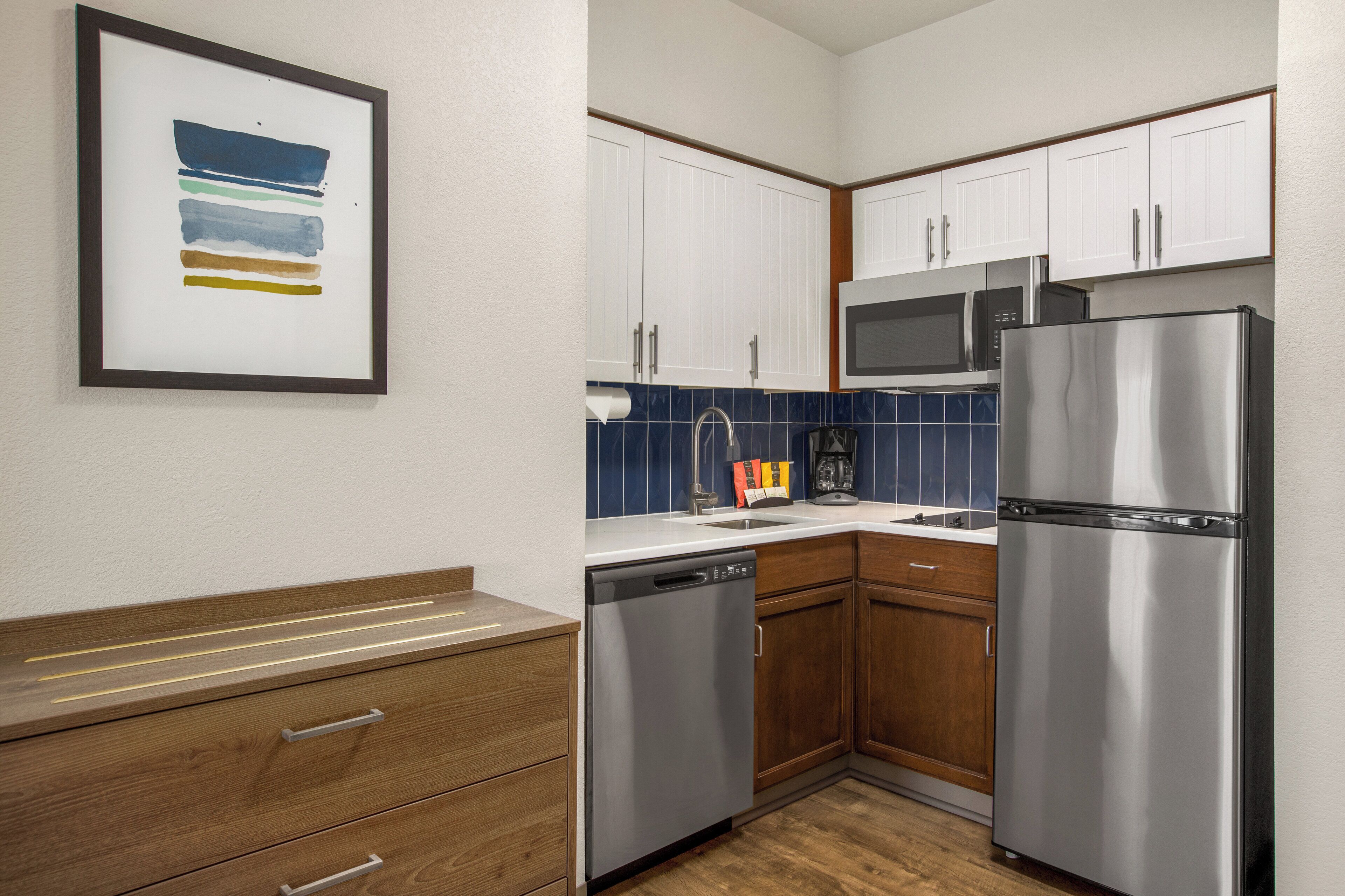 A compact kitchen with white cabinets, a stainless steel refrigerator, a microwave, and a dishwasher.